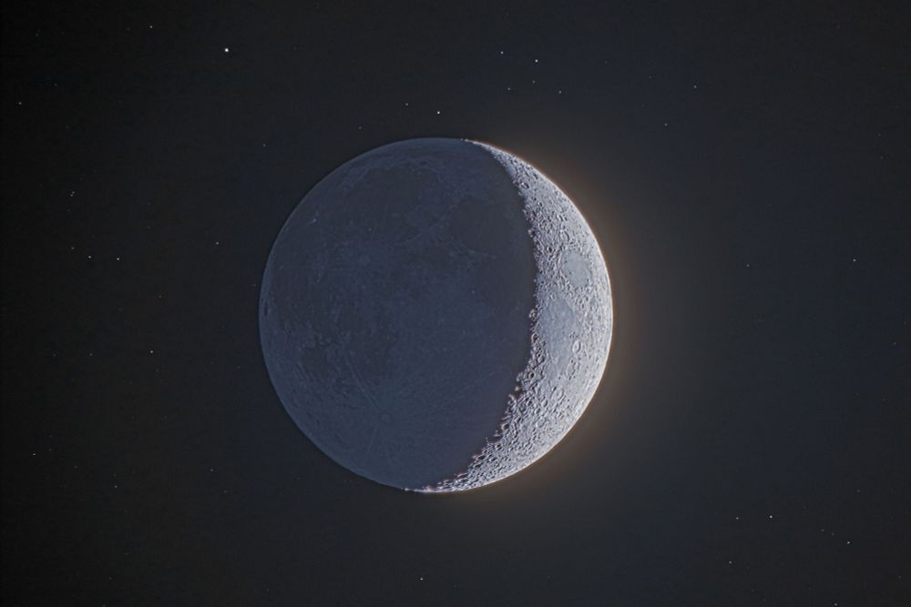 HDR (high dynamic range) image of a crescent Moon with the dark side illuminated by earthshine and several background stars.