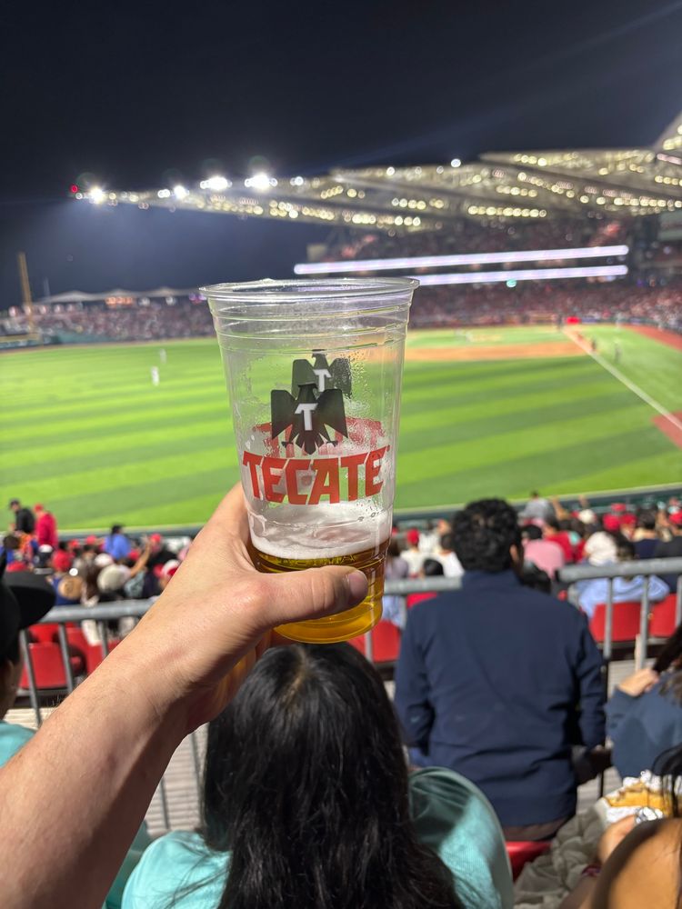 A mostly empty beer at a baseball game, it is a Tecate 