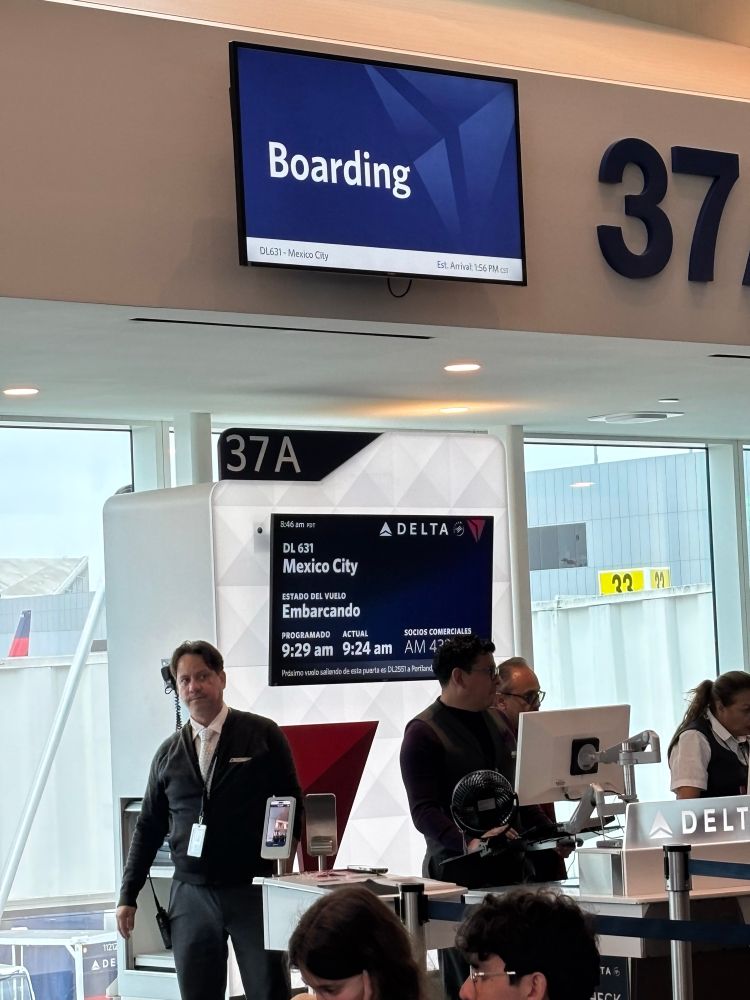 An airport gate area for a flight to Mexico City. The signs show the flight is just about to begin boarding. 