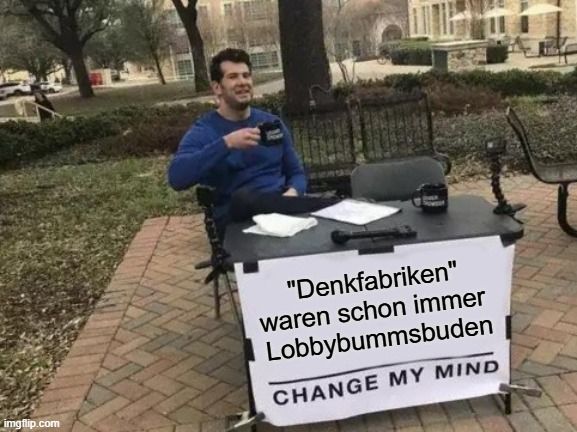 Typ mit Kaffeetasse im Park hinter einem Schild mit "Denkfabriken waren schon immer Lobbybummsbuden" CHANGE MY MIND