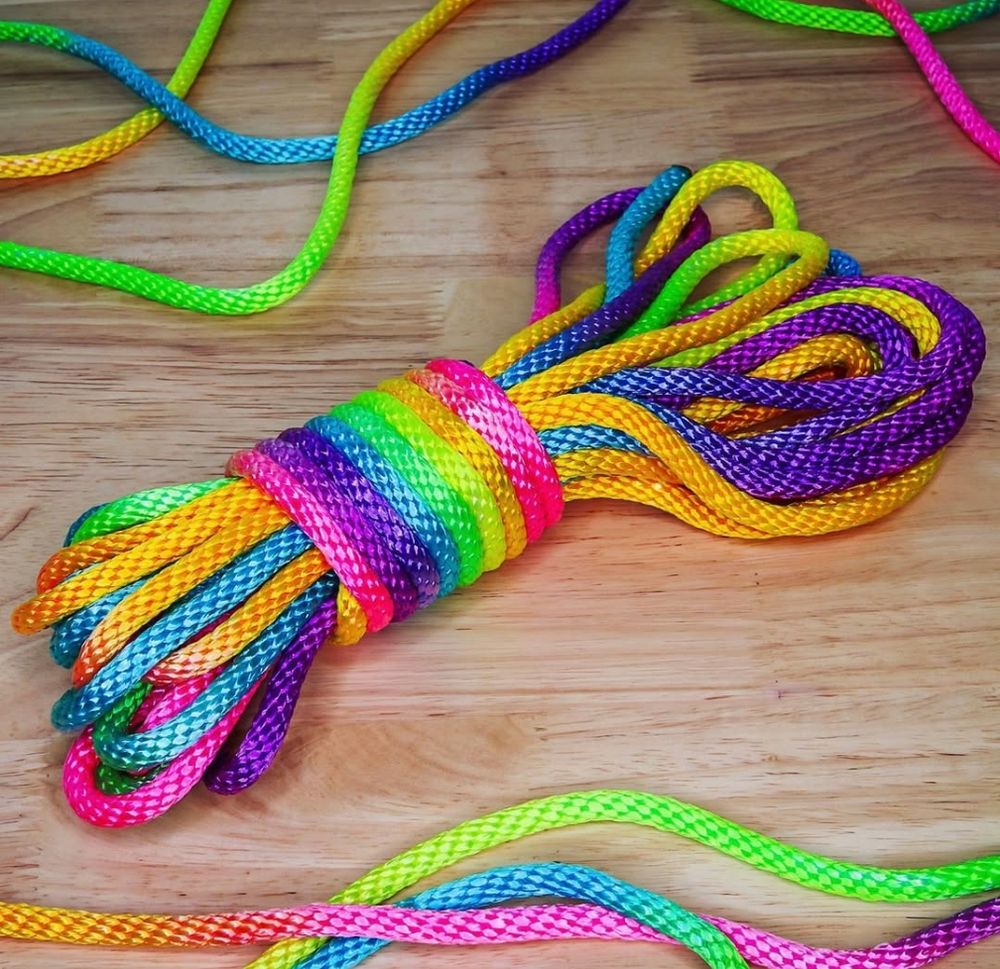 A piece of rope coiled up that is vibrantly colored in pink, purple, blue, green, yellow, and orange on a wooden background. 