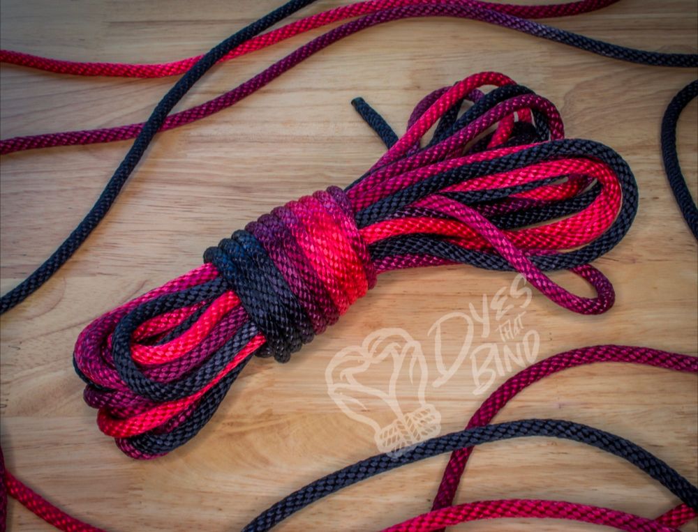 A piece of rope coiled up that is vibrantly colored in deep reds and black on a wooden background. 