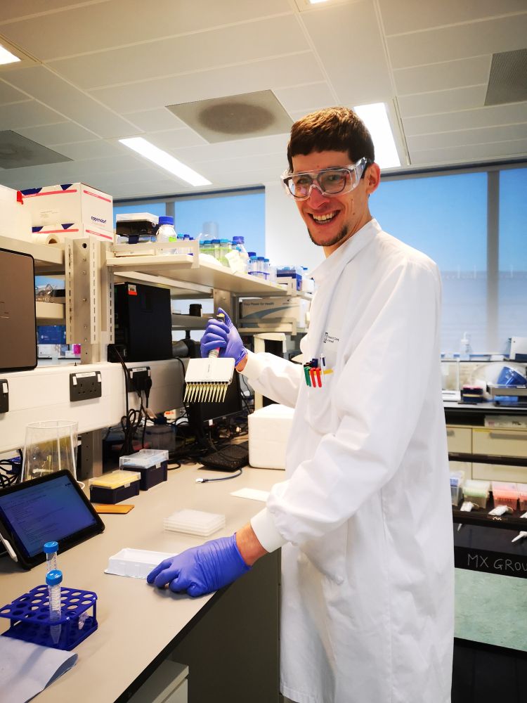 Smiley Hans in the lab wearing proper PPE. Using a multichannel pipette to dispense buffers into a crystallisation plate based on electronic lab notes on a tablet.