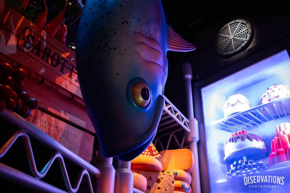 The pantry scene in Remy's Ratatouille Adventure includes a large fish, cheeses, fruits, and a refrigerator filled with pastries