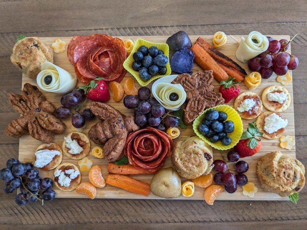 A charcuterie board with the following: 
Cranberry orange muffins shaped like bugs and flowers (our MMC’s deep dark secret). 
Crackers with fig jam and goat cheese (to represent our love interest’s history with one another)
Roasted carrots and potatoes. (for a medieval slant, and for the royal purple hue for our FMC)
Red flowers made out of chorizo, white roses out of provolone, and rosebuds/small flowers made of colby jack. (cause flowers are a thing in this book and charcuterie should have meat and cheese)
Assorted fruit: blueberries, grapes, tangerine butterflies, strawberries (because the mages of this universe must consume fruit to recover when they do a lot of magic).