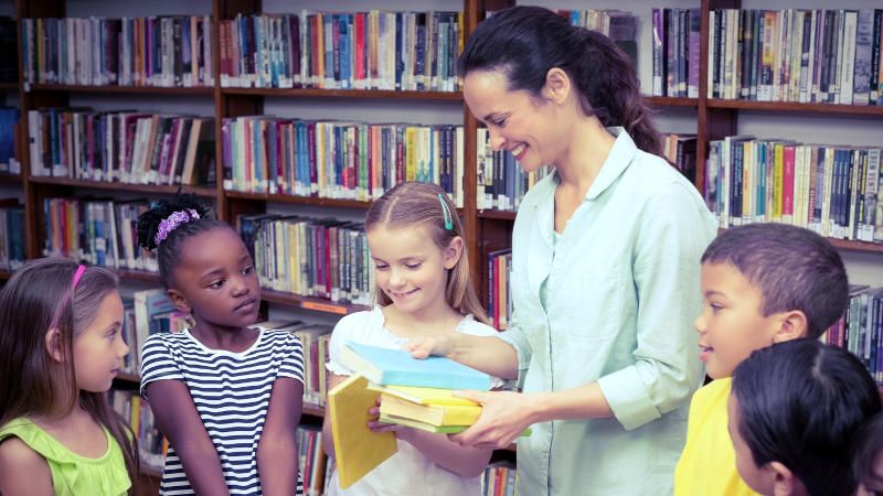 Une enseignante avec des élèves dans la bibliothèque d'une école