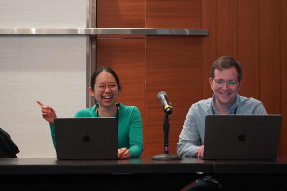 Speakers before session with laptops and mic, one is pointing to screen