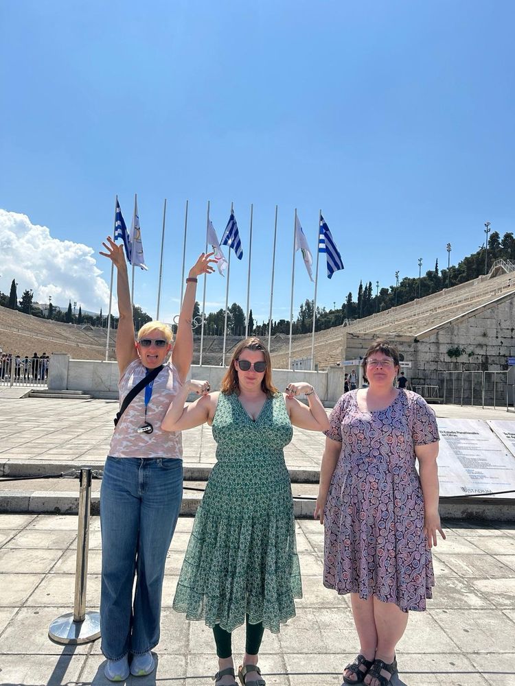 Three middle aged ladies pretend to be columns in front of a historical site that deserves better.