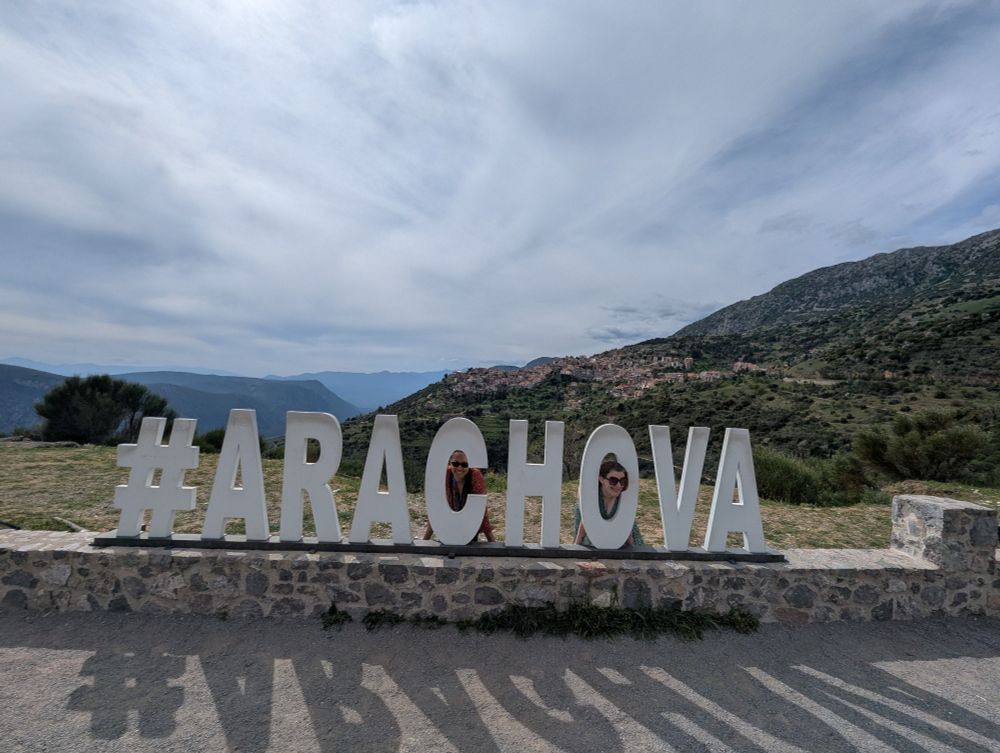 Culliope and her roommate are posing in a big metal sign with 5' tall letters saying #arachova in front of the view of the city 