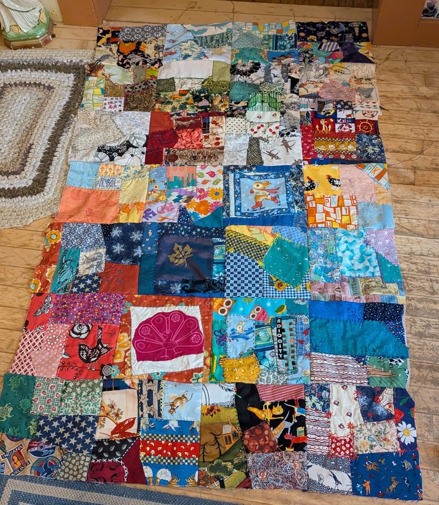 The front of a crazy quilt that is a work in process. There are four squares across by seven squares down. Each square is a collage of different fabrics.