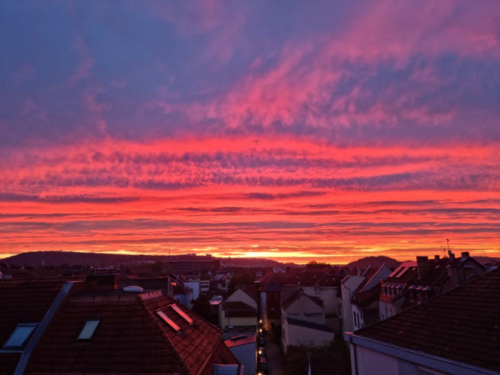 Blick über Häuserdacher in einen flammenden Sonnenaufgang.
Der Himmel füllt die oberen 2/3 des Bildes.