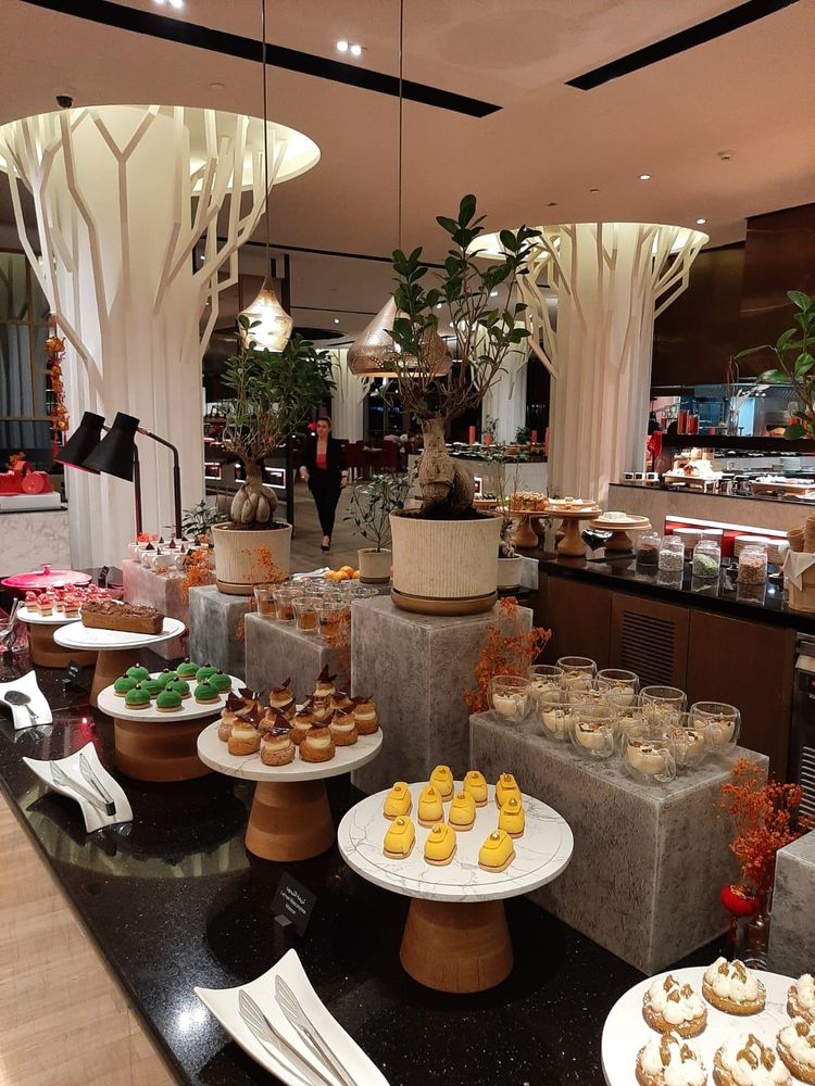 Buffet met veel verschillende kleine glaasjes en gebakjes. In de eetzaal staan diverse witte pilaren in de vorm van boomstammen