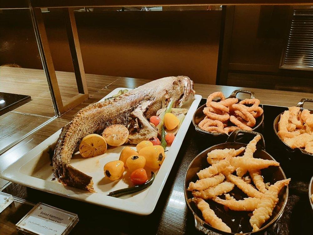 Hele zeebaars op een schaal met daarnaast nog enkele schaaltjes met vishapjes