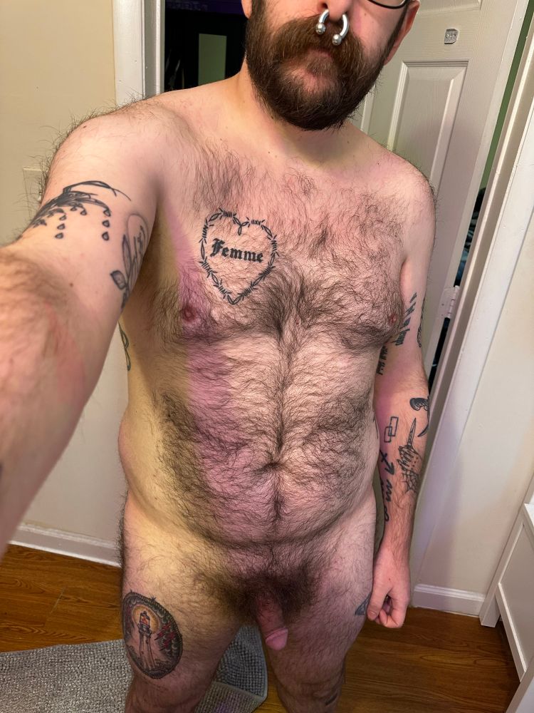 a hairy cub with tattoos and a stretched septum standing in their bathroom with a softie 