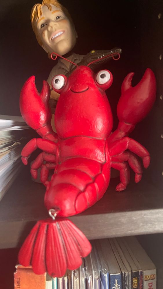 A wooden lobster sitting on a bookshelf. 