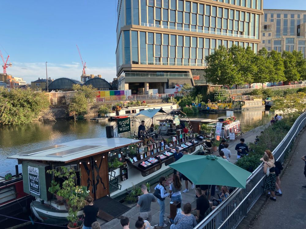 „Word on the Water“-Buchladen auf einem Boot auf dem Regent‘s Canal im Abendlicht. Auf dem Boot sitzt ein Pianist, davor stehen einige Menschen.
