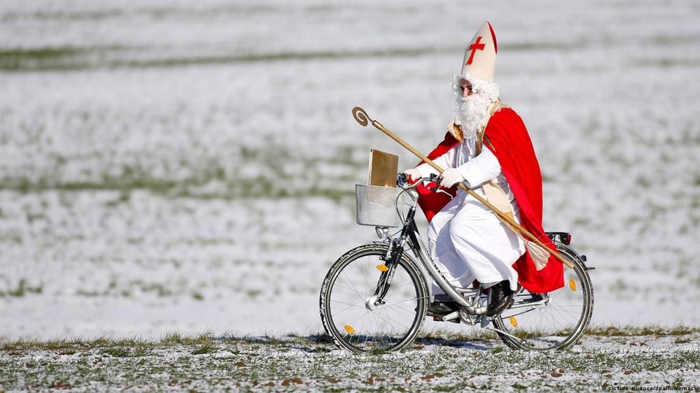 Eine Person mit Nikolaus Anzug fährt mit einem Fahrrad durch ein verschneiten Landschaft.