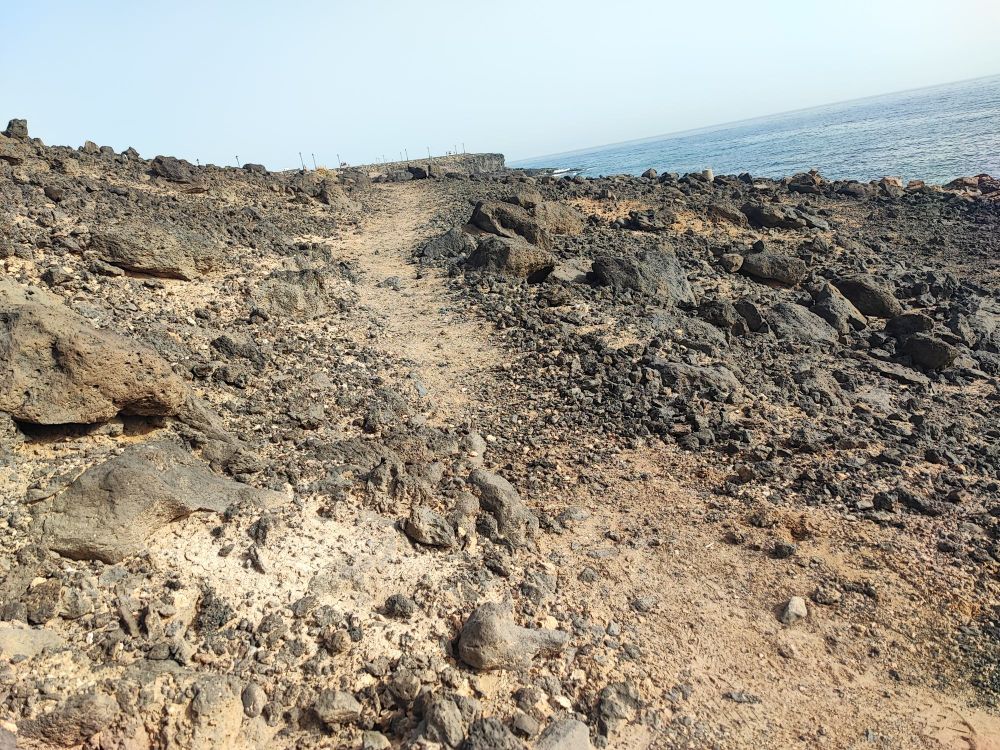 Ein Wanderweg slamomt sich zwischen den lavasteinen. Rechtsoben ist der Atlantik 