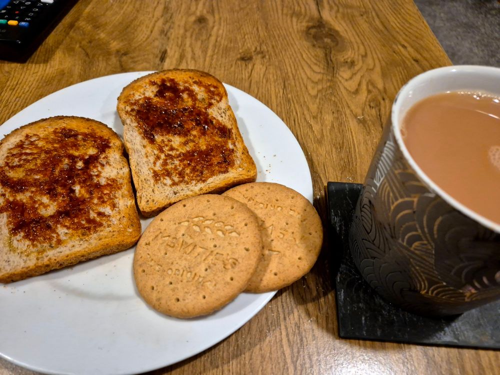 Two slices of Marmite on wholemeal toast, and two McVitie's digestive biscuits on a white plate, next to a big mug of tea with milk.