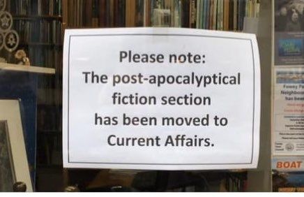 Photograph of a sign in the window of a bookshop (Bookends, Fowey) reading 'Please note: The post-apocalyptic fiction section has been moved to Current Affairs'