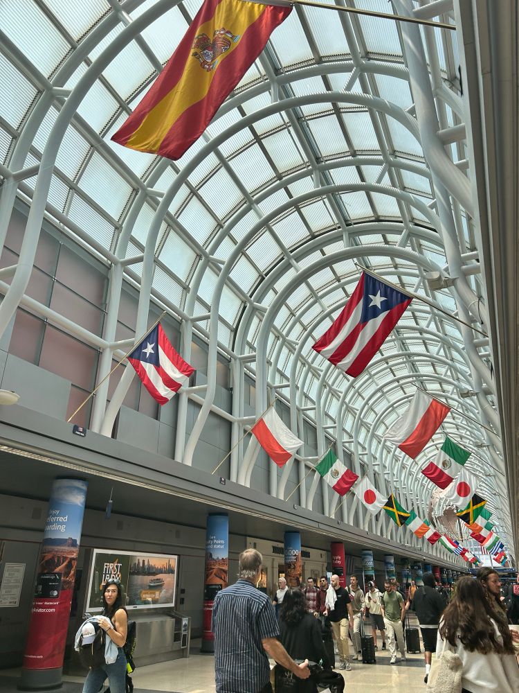 Airport terminal displaying flags from around the world. The Puerto Rican flag is in the foreground.