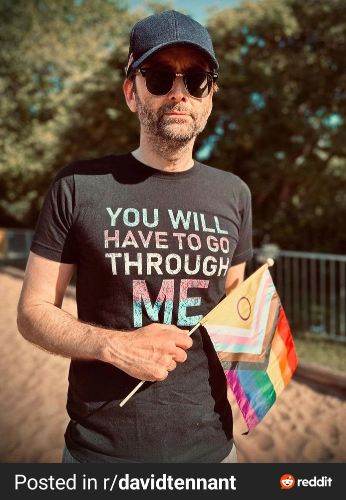 Photo of David Tennant wearing a shirt that says "you will have to go through me" in trans flag colors