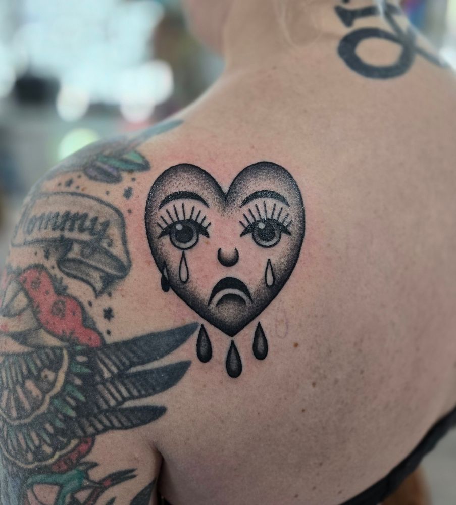 a fresh traditional style tattoo of a crying black and grey heart. near some older american traditional style tattoos, which aren't my work. 