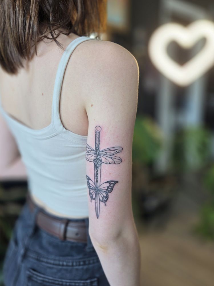 a fresh tattoo of a dagger, with a dragonfly and a butterfly 