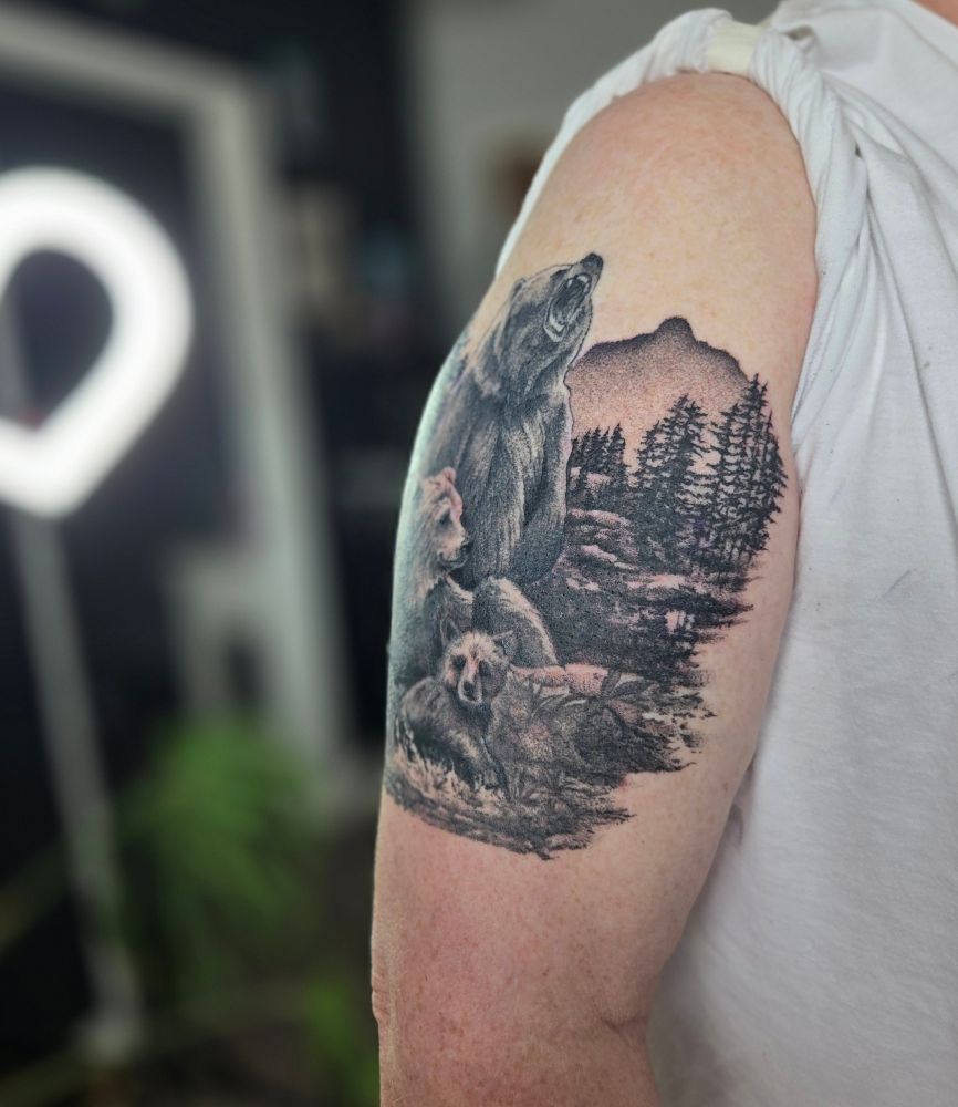 a black and grey tattoo, featuring a family of 3 bears which are surrounded by trees and mountains