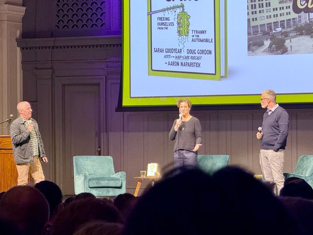 Doug Gordon, Sarah Goodyear, and Ray Delahanty stand on a stage and talk with each other about urbanism and the new book
