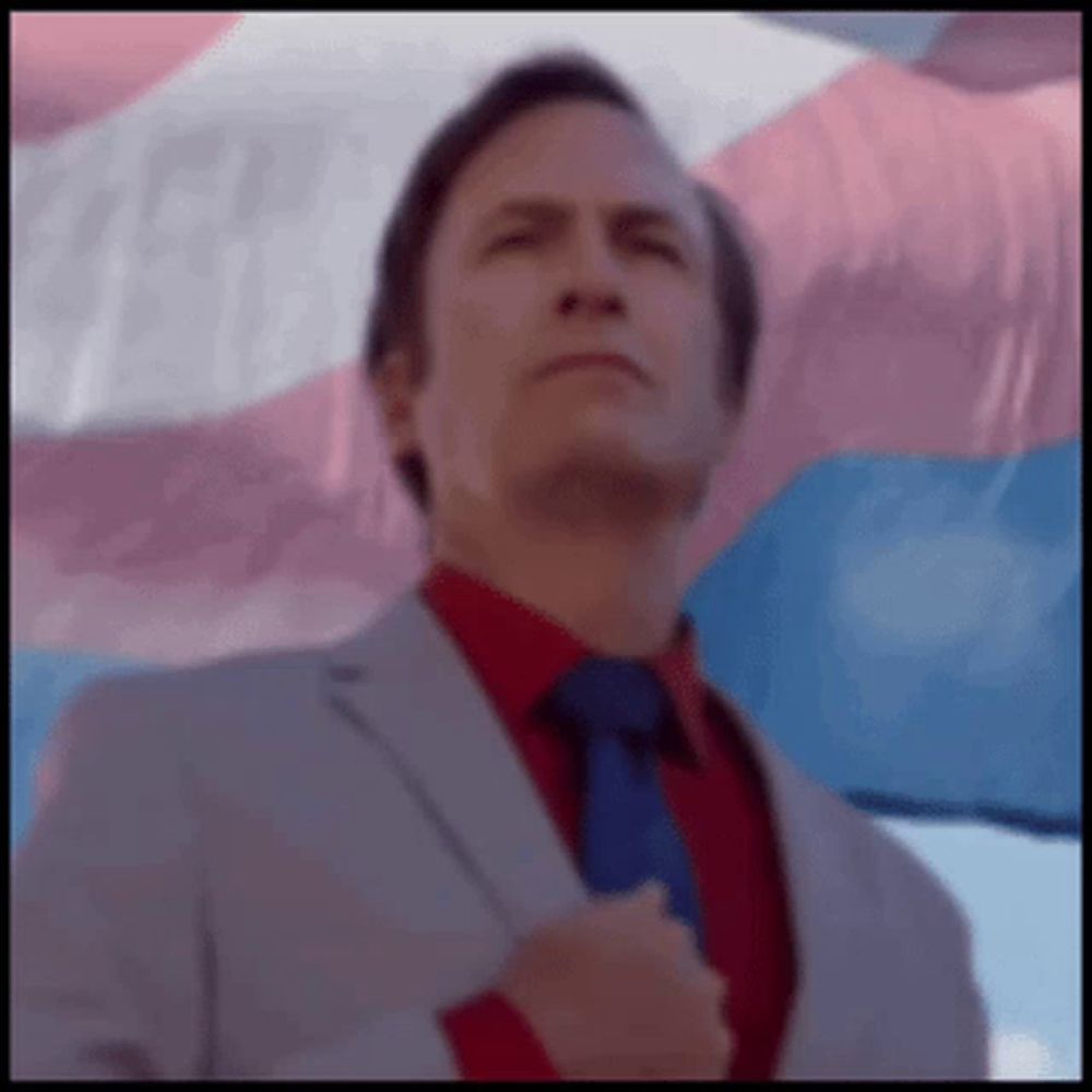 a man in a suit and tie standing in front of a transgender flag .