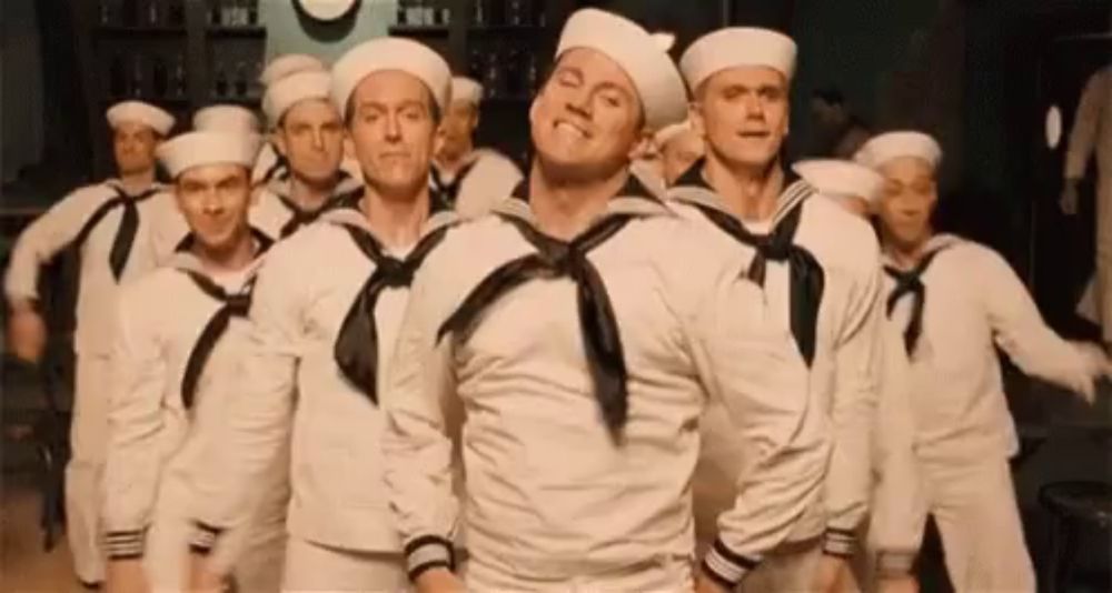 a group of sailors are dancing in a line in a room .