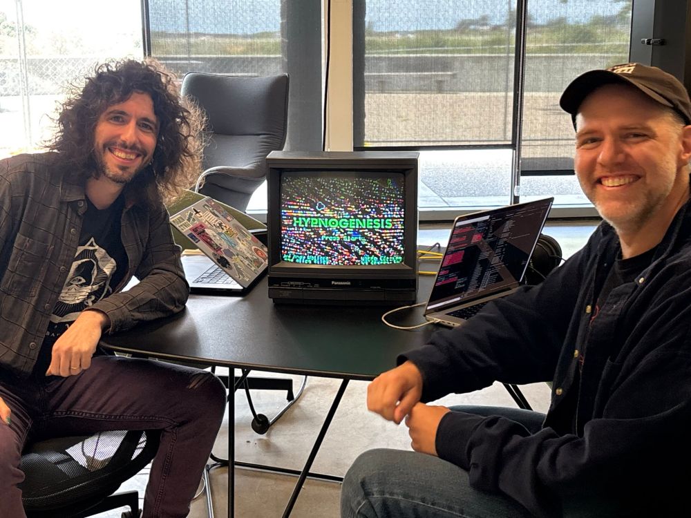 Two wonderful and alluring men sitting on either side of a CRT that says "HYPNOGENESIS"
