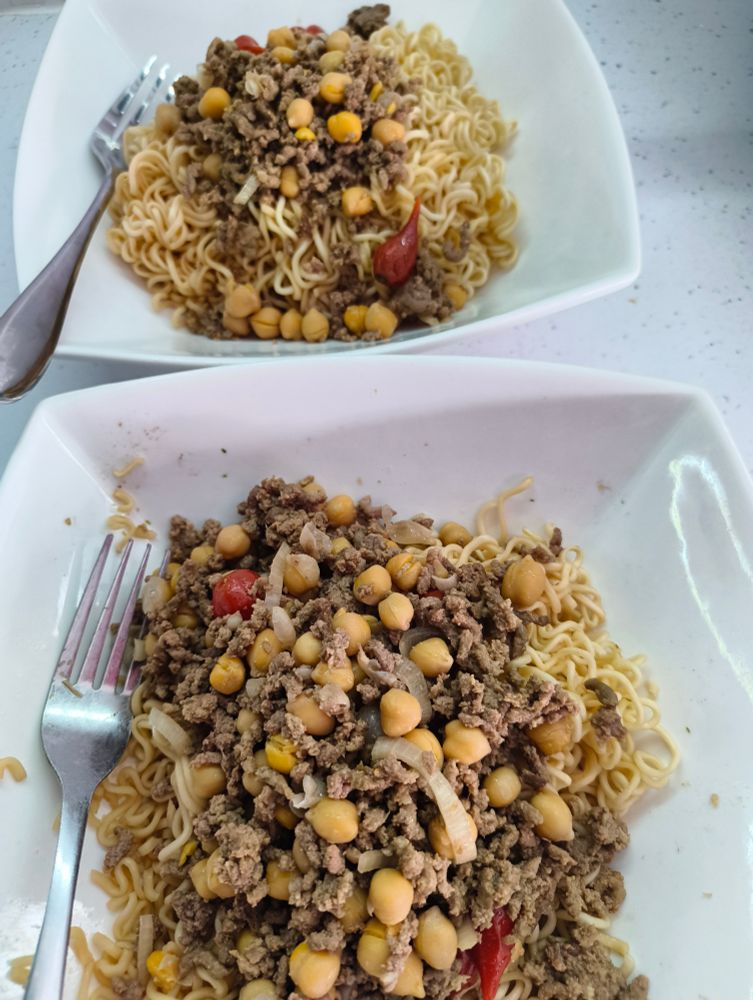 Two bowls with forks, minced beef, chick peas, kecap manis, shallot, Peppadew piquant peppers, garlic, served on sesame noodles