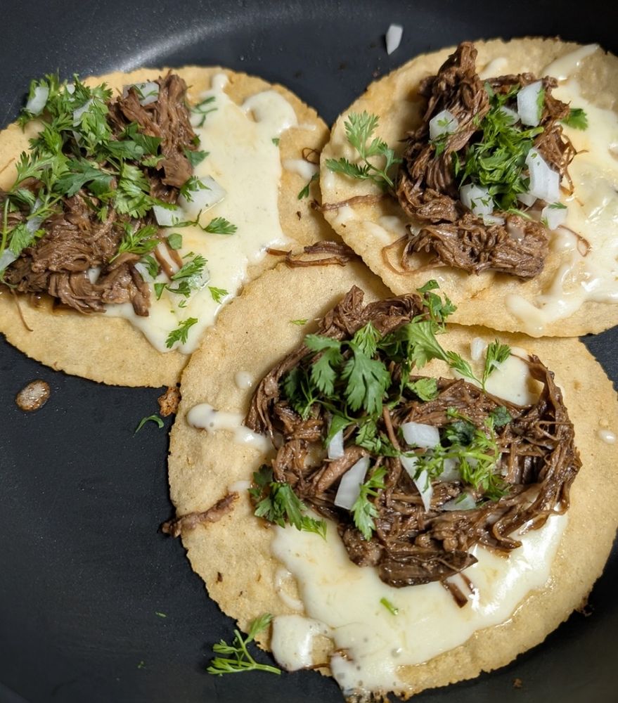 In a skillet are three homemade tortillas with beef birria, onions and cilantro and shredded Monterey Jack cheese. They will be fried lightly and then folded.