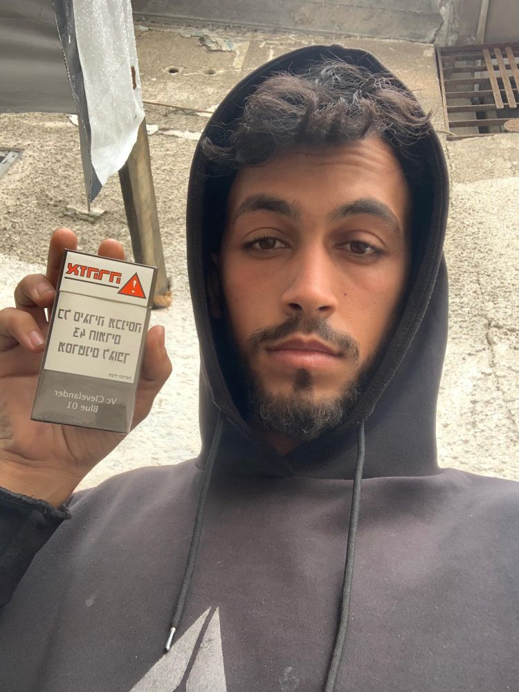 Mohammed Shobair, 23 years old, from Gaza, holding a pack of cigarettes with writing in Hebrew.