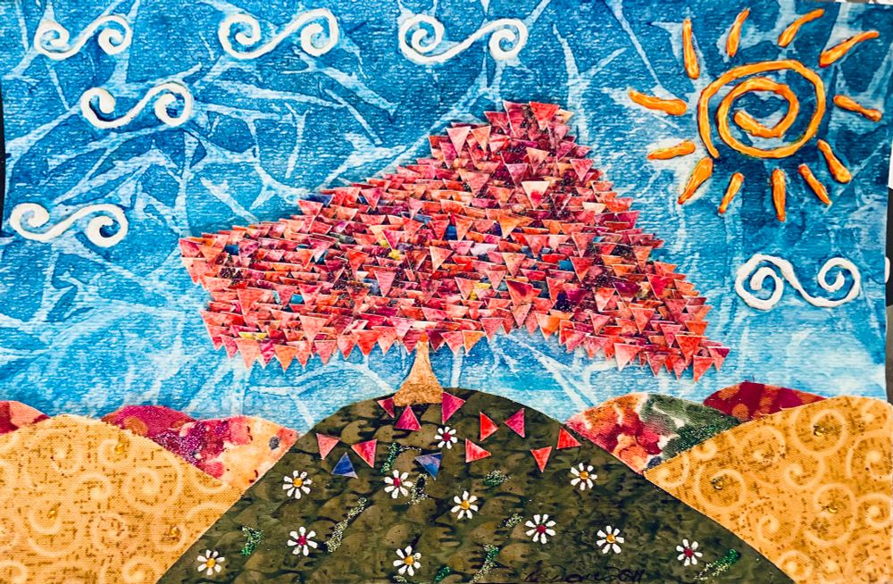 Mixed media piece on watercolour paper of a pink tree with leaves made of tiny cut out triangles. It stands on a green fabric hill with white flowers on it. The hills that surround it are gold fabric with swirls on them, and multicoloured ones in the distance. There is a stylized spiral sun and stylized swirl clouds on a blue textured sky. 