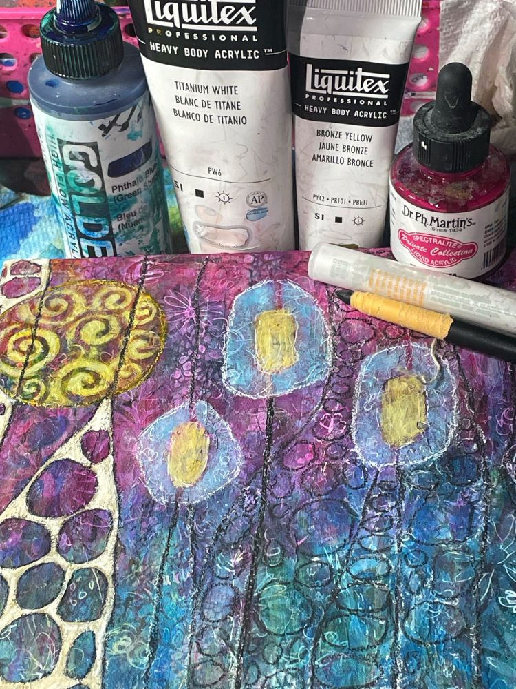 Work in progress abstract painting in pinks, blues, and yellows, with a circle theme. 
Paints and mark making tools are behind it. 