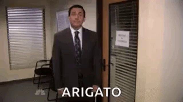 a man in a suit and tie is standing in front of a door with the word arigato on it .