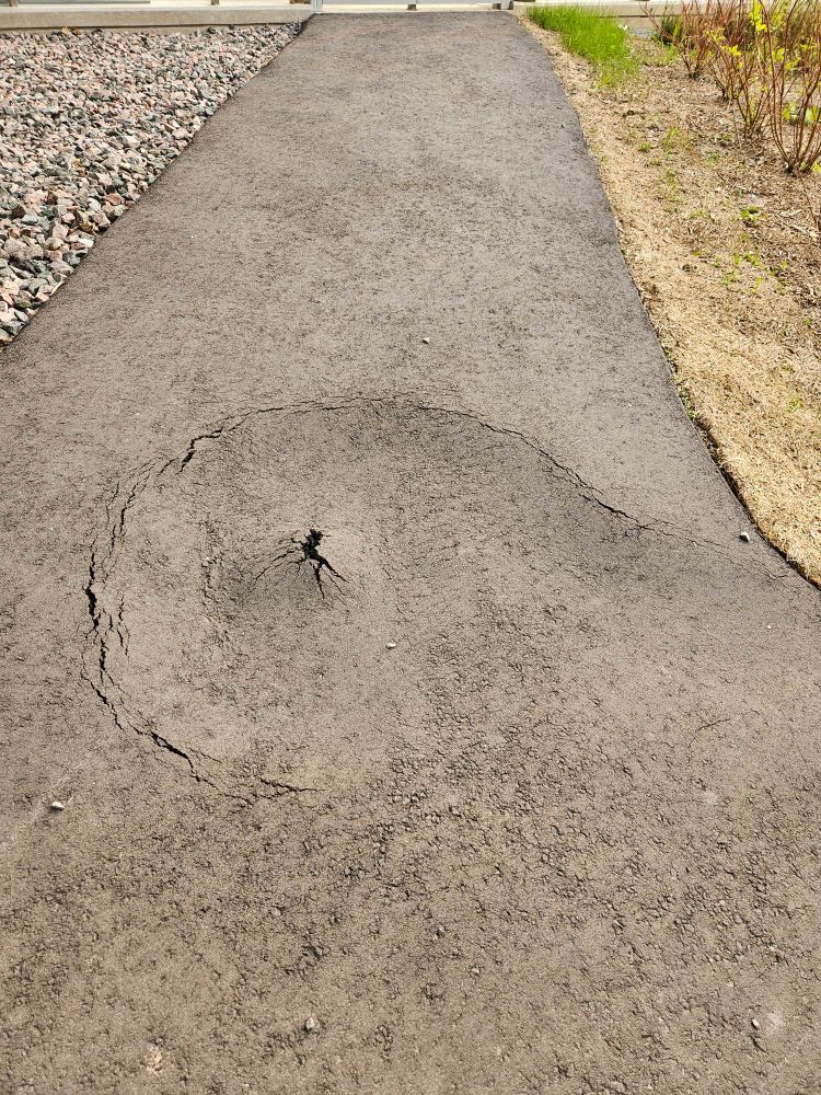 A sunken volcano cone of asphalt about 2 feet wide in the middle of a paved pathway. 