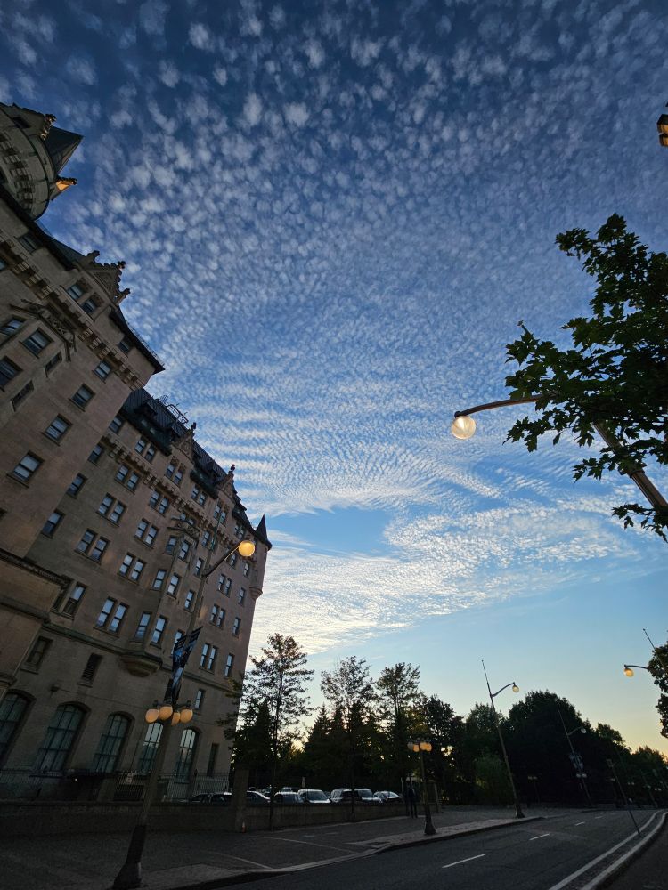White dappled clouds in a blue sky, over a Gothic style stone building. 