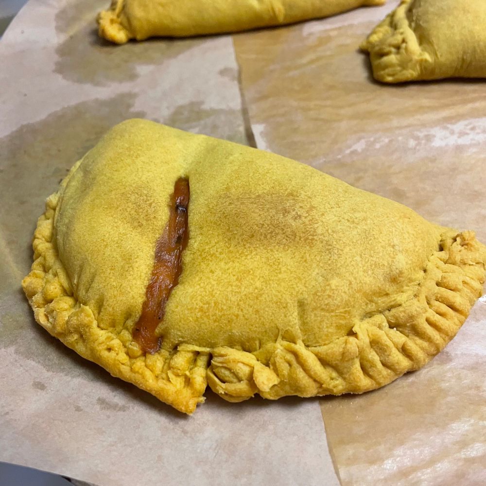 Close-up of a Jamaican patty with curry filling oozing slightly from the slash in the middle.