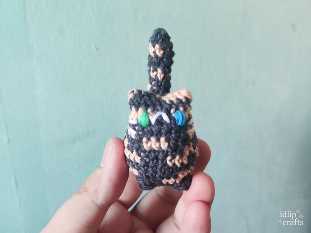a lighter orange tortoiseshell cat amigurumi with green blue heterochromia 