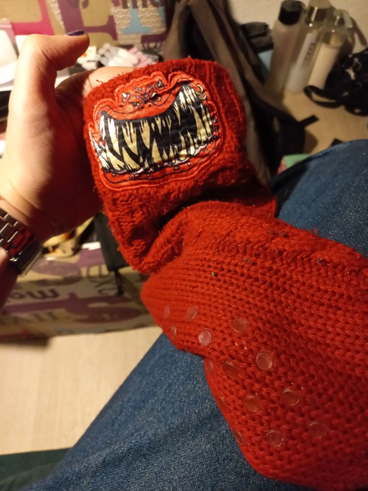 A big red sock with the face of a squig on it. It has some small plastic circles on the soles.