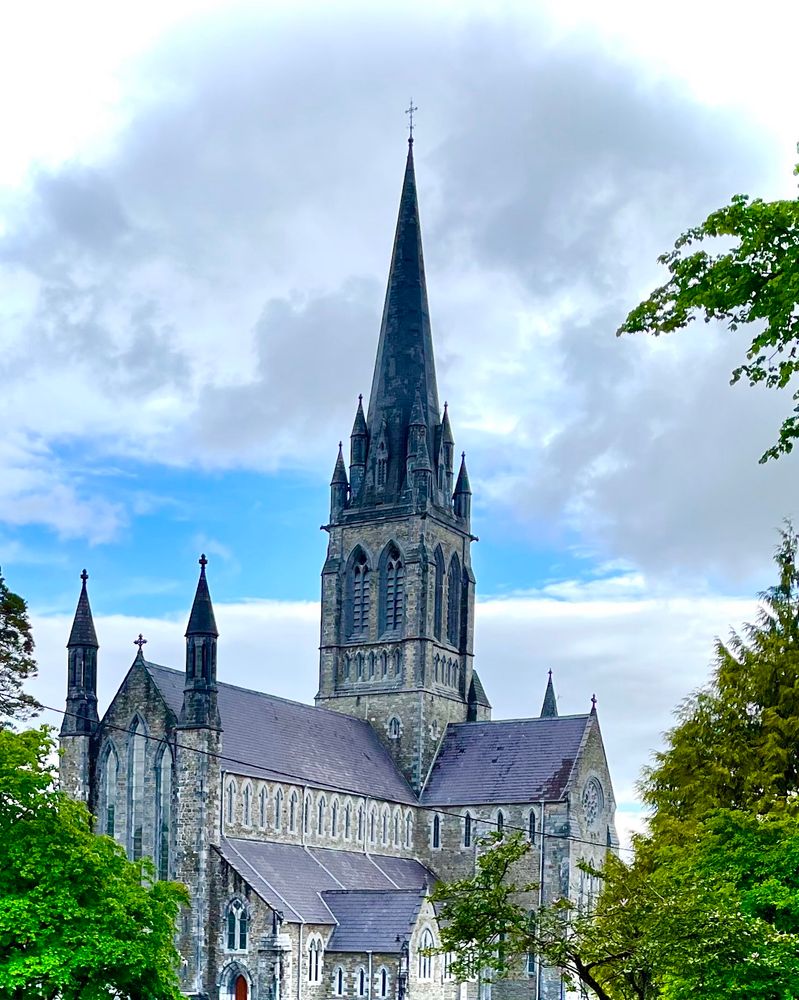 A cathedral set against a blue sky with fluffy clouds and trees around the perimeter 