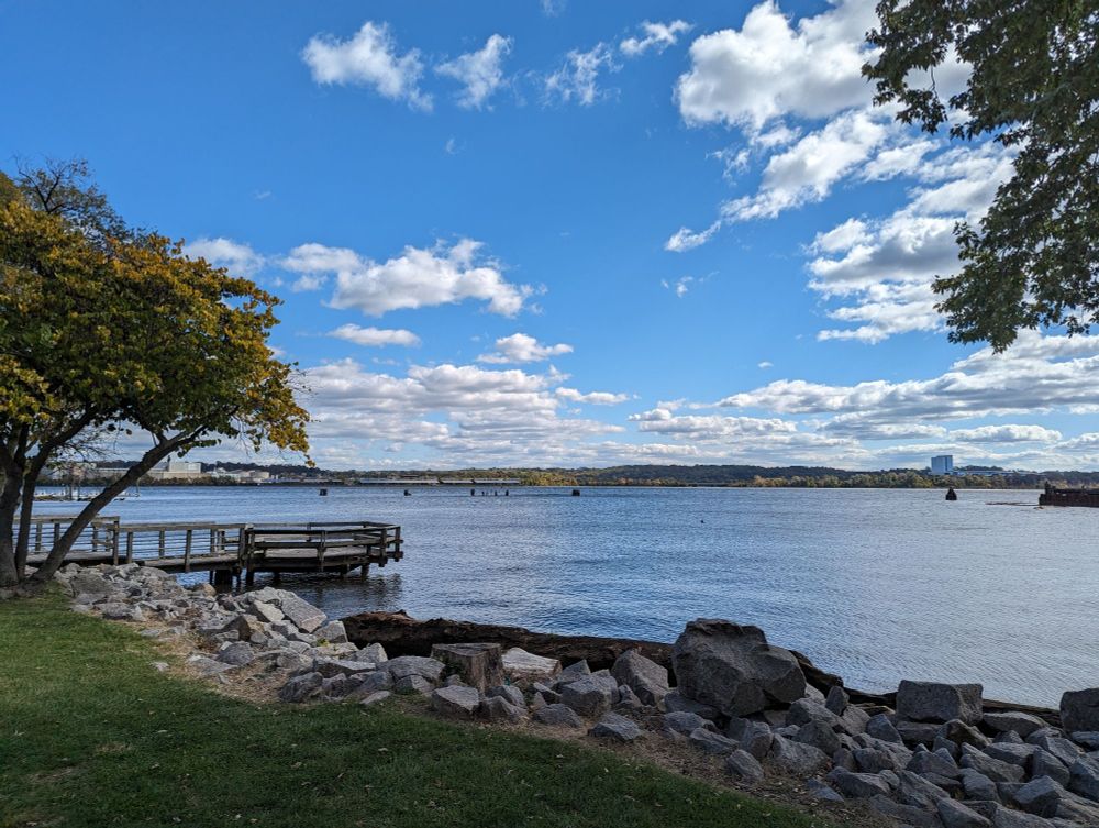 The Potomac River under blue, speckled skies, with trees and rocks in the foreground.