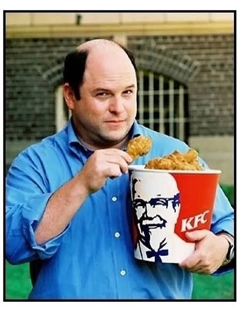 Jason Alexander holding a bucket of KFC chicken in one arm and a drumstick in the other hand