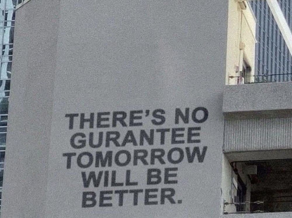 A photo of the side of a building. Them text superimposed on it reads: THERE'S NO GURANTEE TOMORROW WILL BE BETTER.