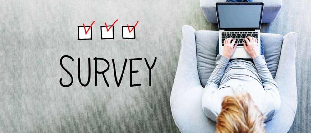 Overhead photograph of a woman sitting on a chair completing the Centre's survey on a laptop. The word SURVEY is included along with three ticks in red ink.