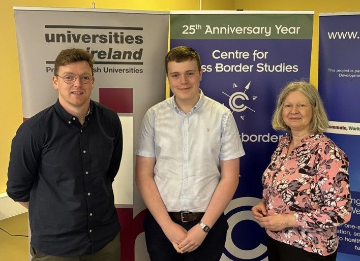 Photograph of James with Mark and Lisa in the Centre's meeting room. In the background are three pull-up stands representing Universities Ireland, the Centre, and the Border People project.